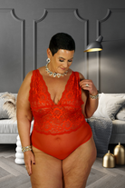 Plus size red lace bodysuit worn by woman with short hair and silver jewelry in stylish living room